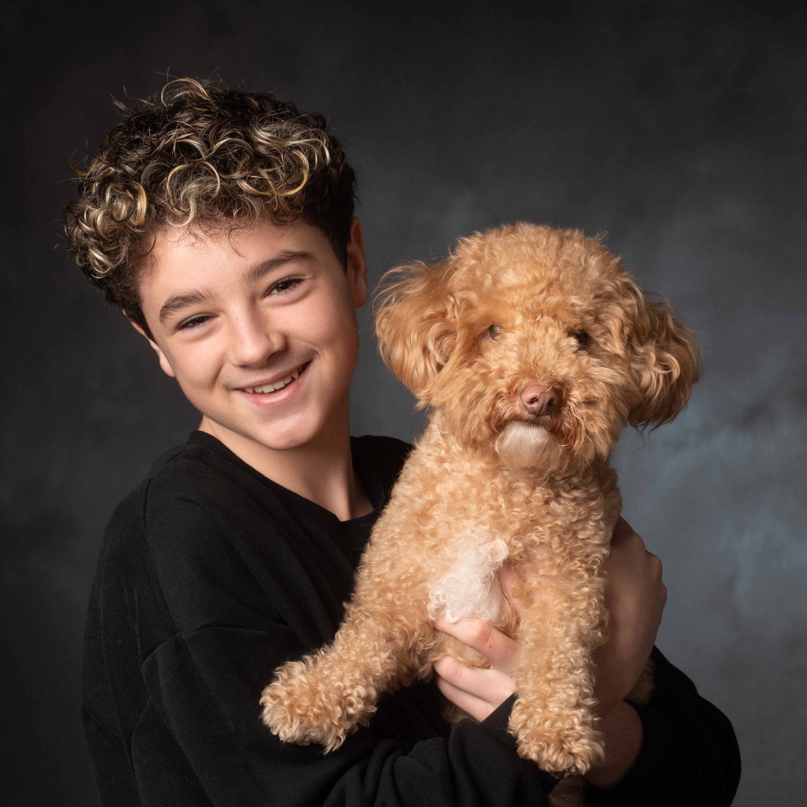 Young boy holding a small brown dog against a dark background