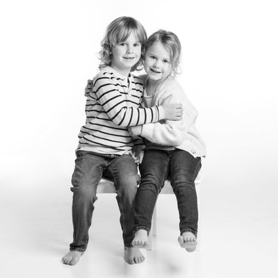Black and white image of Two children sitting on a white chair against a white background