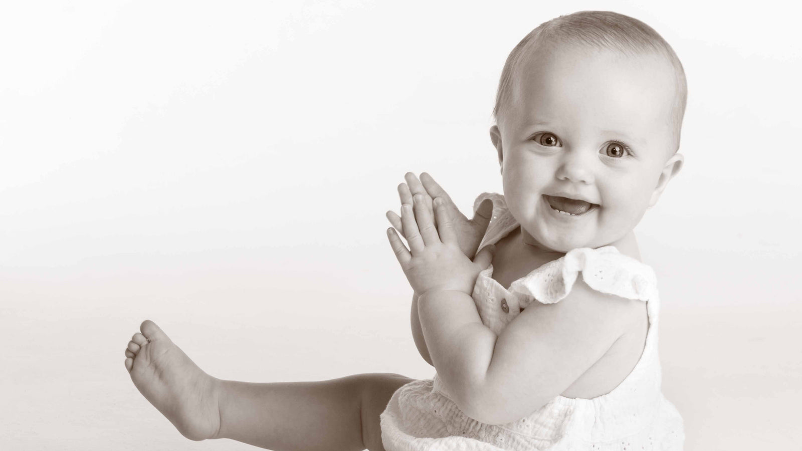 Black and white photo of a baby sitting on a white background