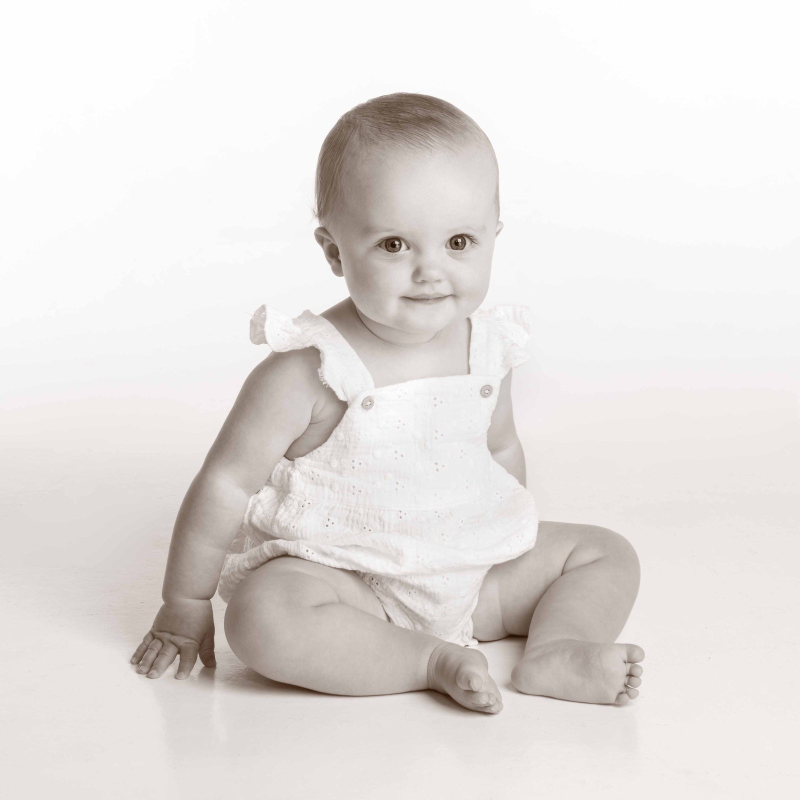 Black and white photo of a baby sitting on a white background