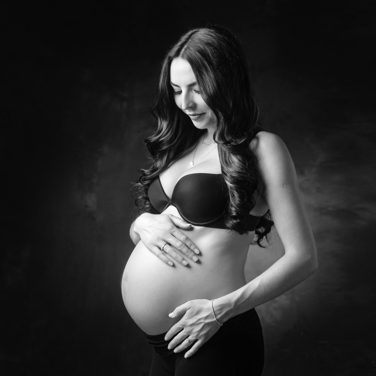 Black and white photo of a pregnant woman holding her belly against a dark background